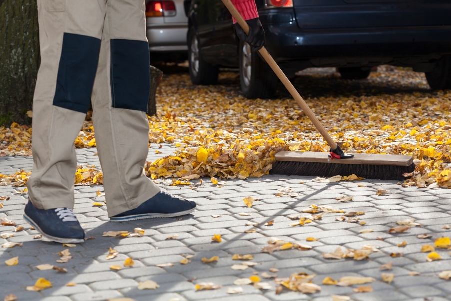 A man sweeping leaves off a driveway with a broom